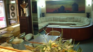 A living room with a curved sofa, a dining table with chairs, and a large painting on the wall. - Claridge Hotel (Athens)
