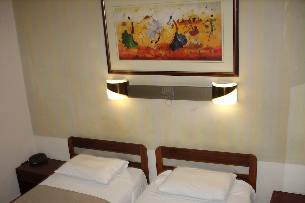 A hotel room with two beds, a painting on the wall, and two wall-mounted lights.