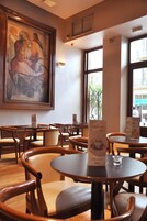 Un café avec des tables et des chaises en bois, un grand tableau encadré au mur et un présentoir à menus.