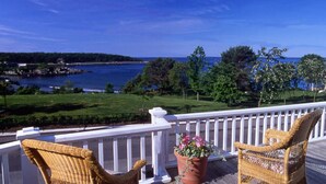 A balcony with wicker chairs and a potted plant, overlooking a body of water and greenery. - York Harbor Inn (York Harbor)