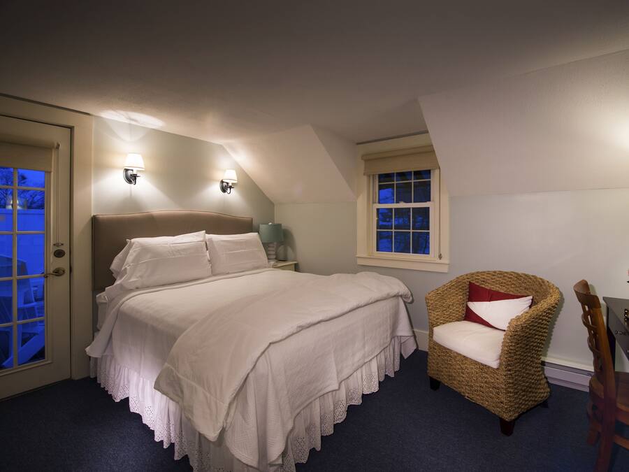 A bedroom with a bed, a chair, a desk, and a window.
