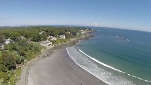 An aerial view of a coastal area with a sandy beach, a rocky shoreline, and a row of houses with large windows overlooking the ocean. - York Harbor Inn (York Harbor)
