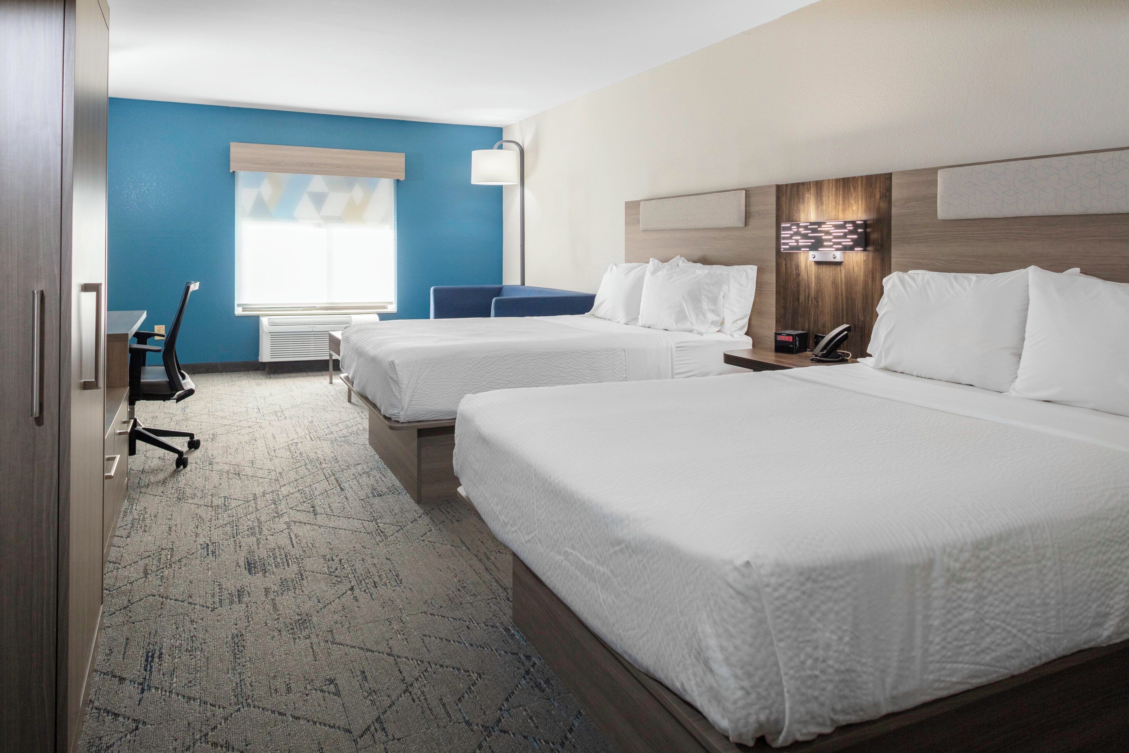 Habitación de hotel con dos camas, un escritorio, una silla y un ventanal con persianas.