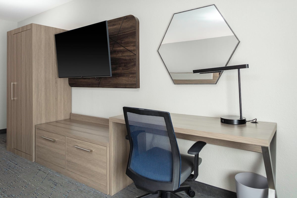 A modern room with a wooden desk, a computer, a chair, a television, and a mirror.