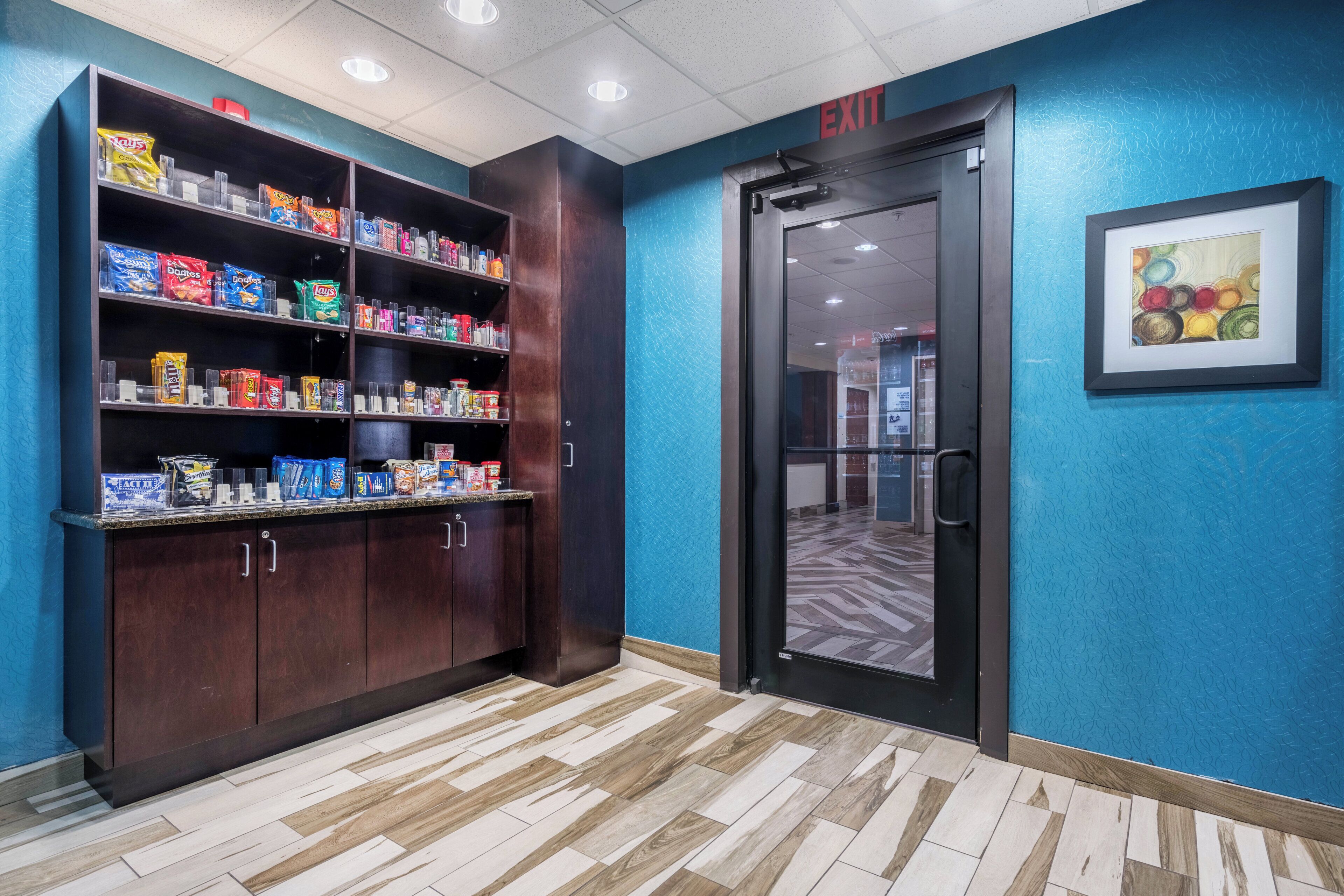 A hallway with a snack shelf stocked with various chips and a door marked 'EXIT'.