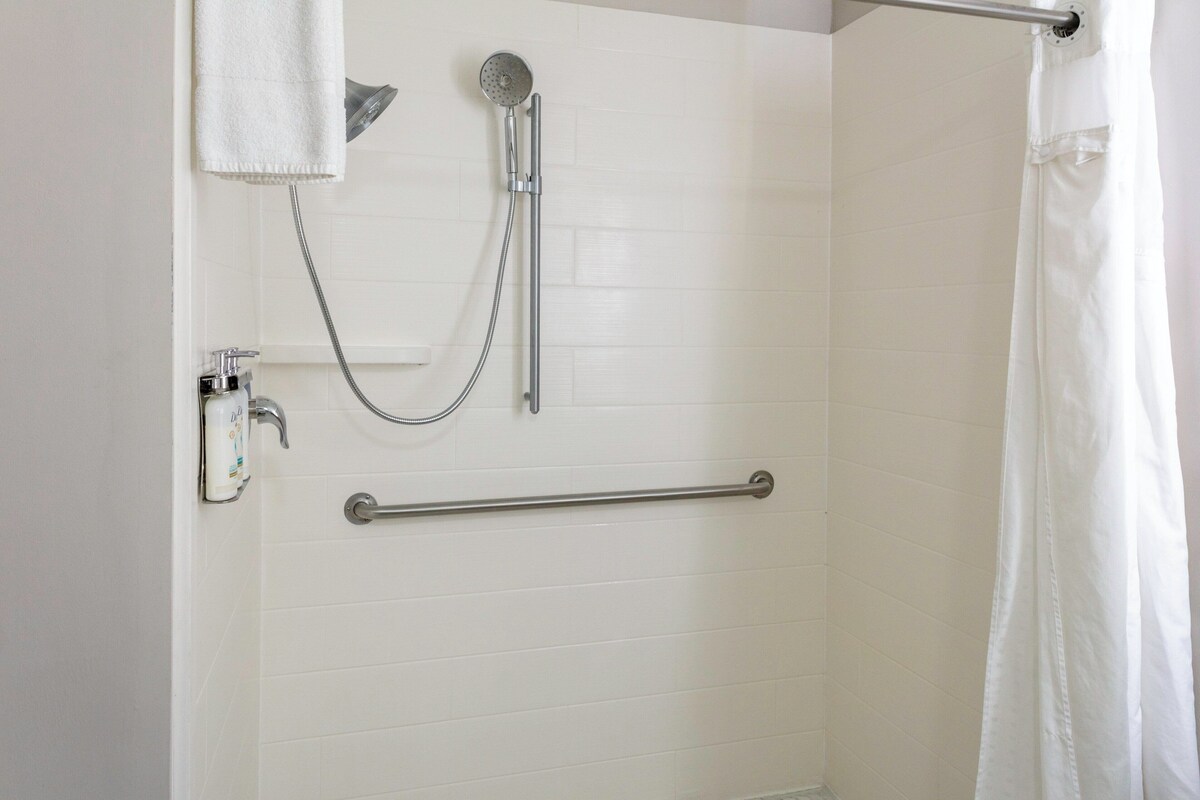 A shower with a handheld showerhead, a handheld shower attachment, and a grab bar.