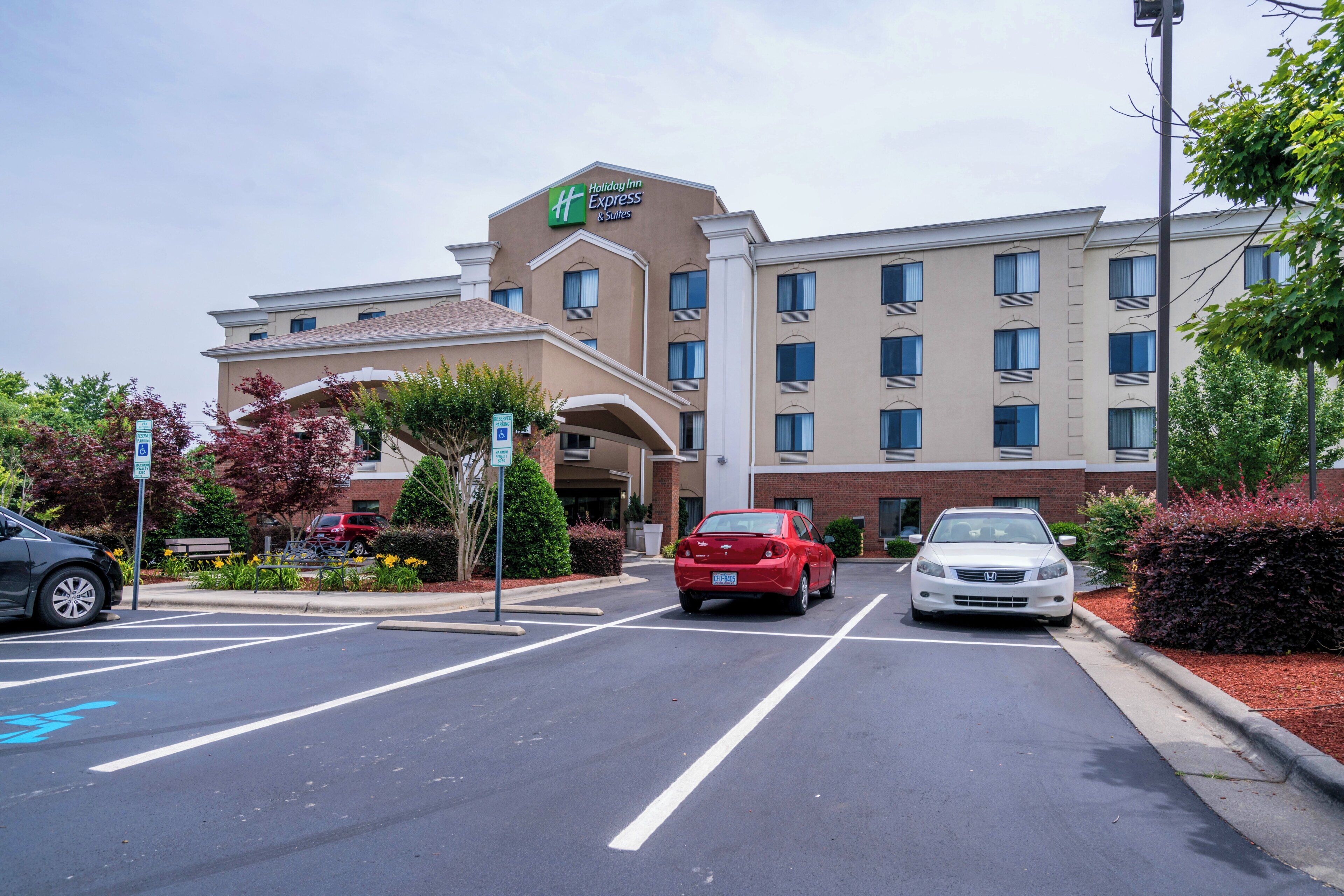 A Holiday Inn Express & Suites hotel with a parking lot, a red car, and a white car parked in front.