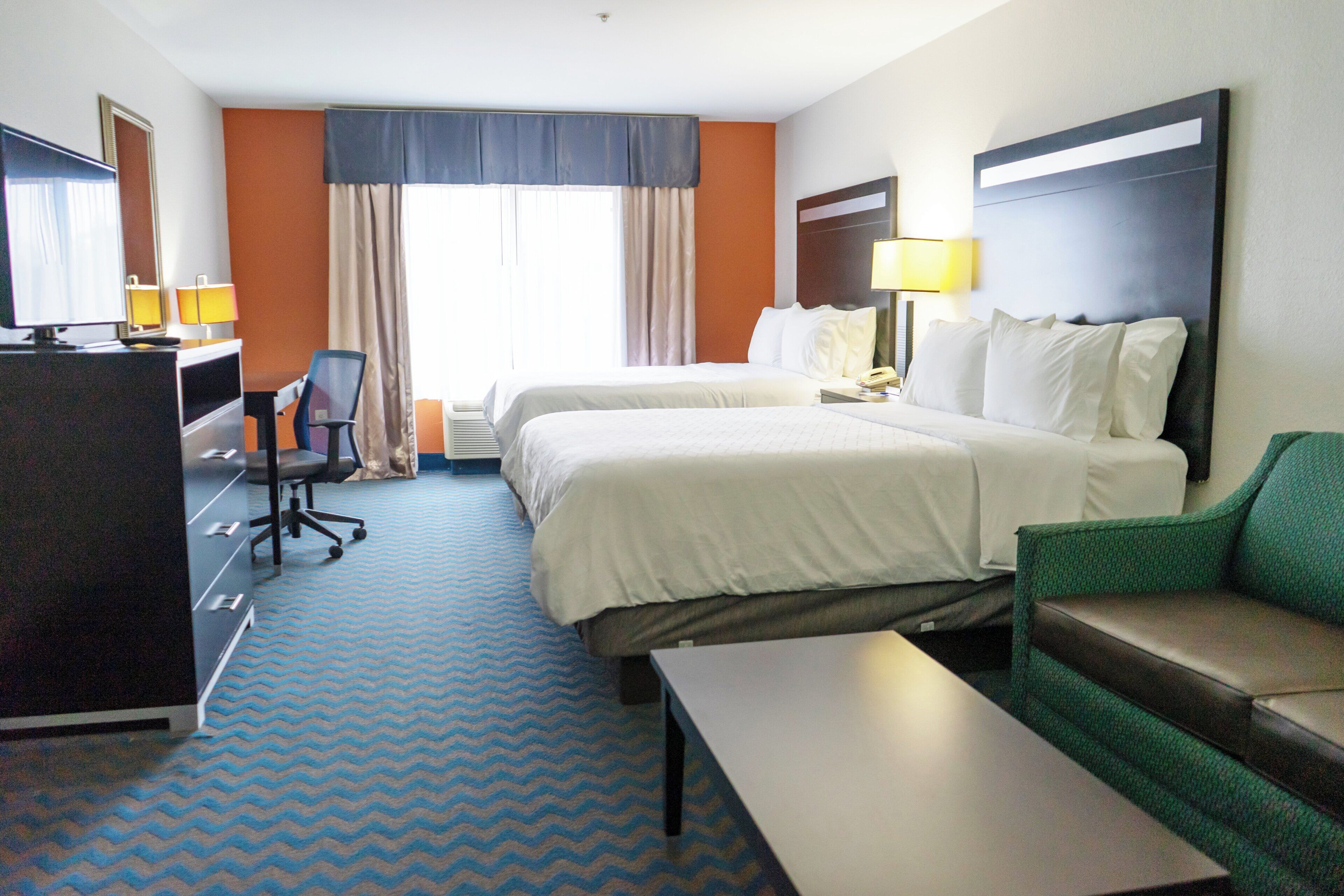 A hotel room with two beds, a desk, a chair, a TV, and a sofa.