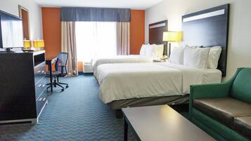 A hotel room with two beds, a desk, a chair, a TV, and a sofa.