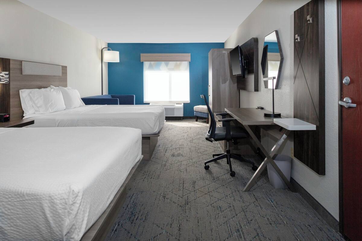 A hotel room with two beds, a desk, a chair, a TV, and a window with blinds.
