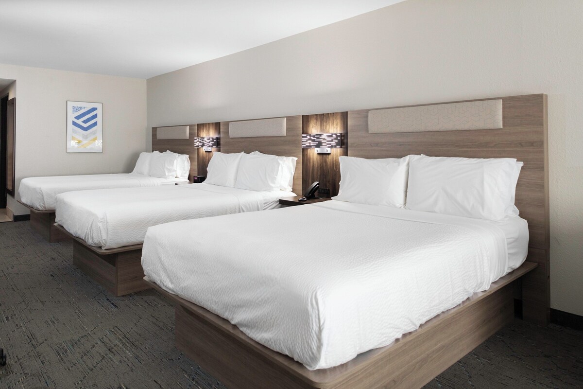 A hotel room with two beds, a headboard with integrated lighting, and a carpeted floor.