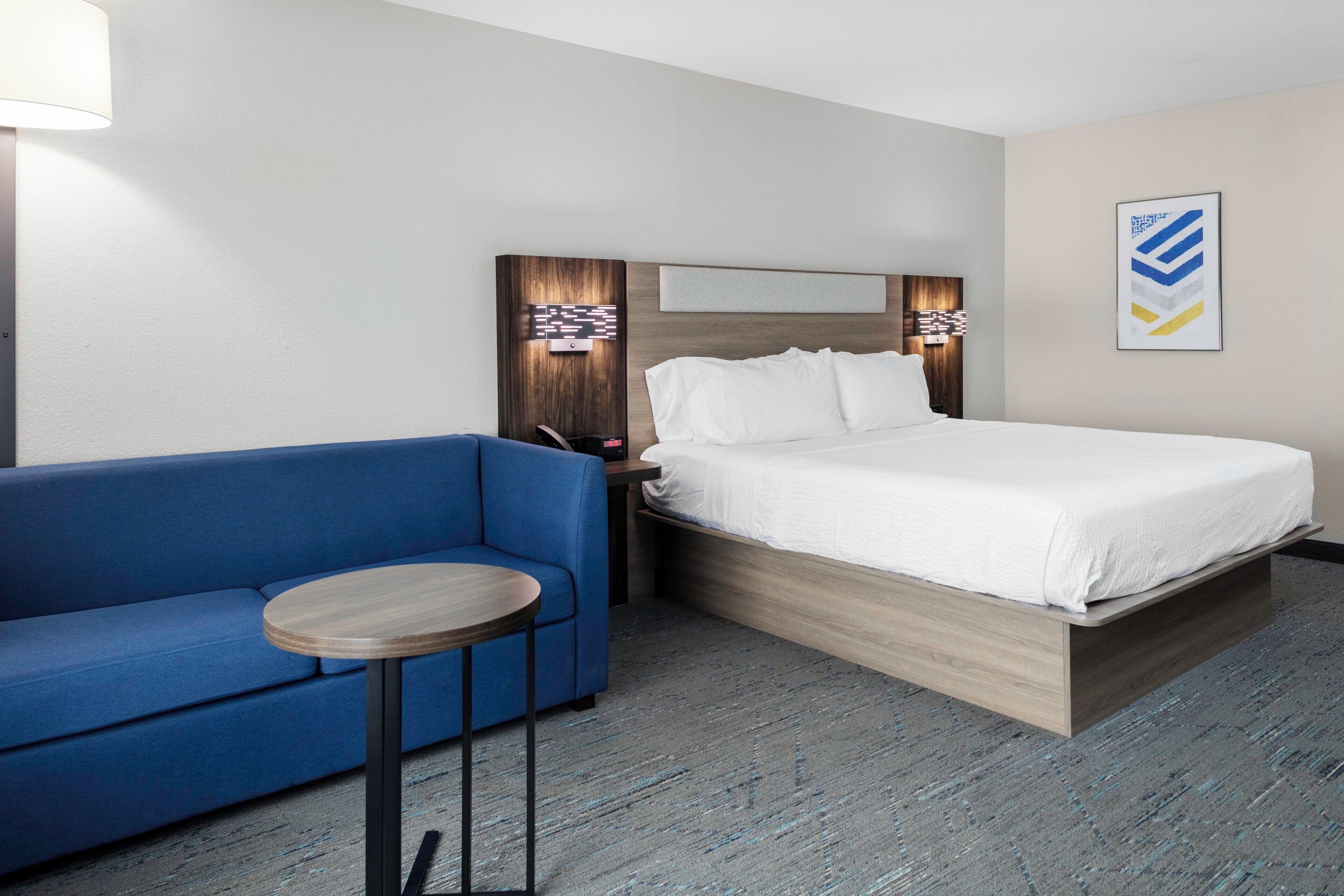 A hotel room with a bed, a blue sofa, a small round table, and a wall-mounted light fixture.
