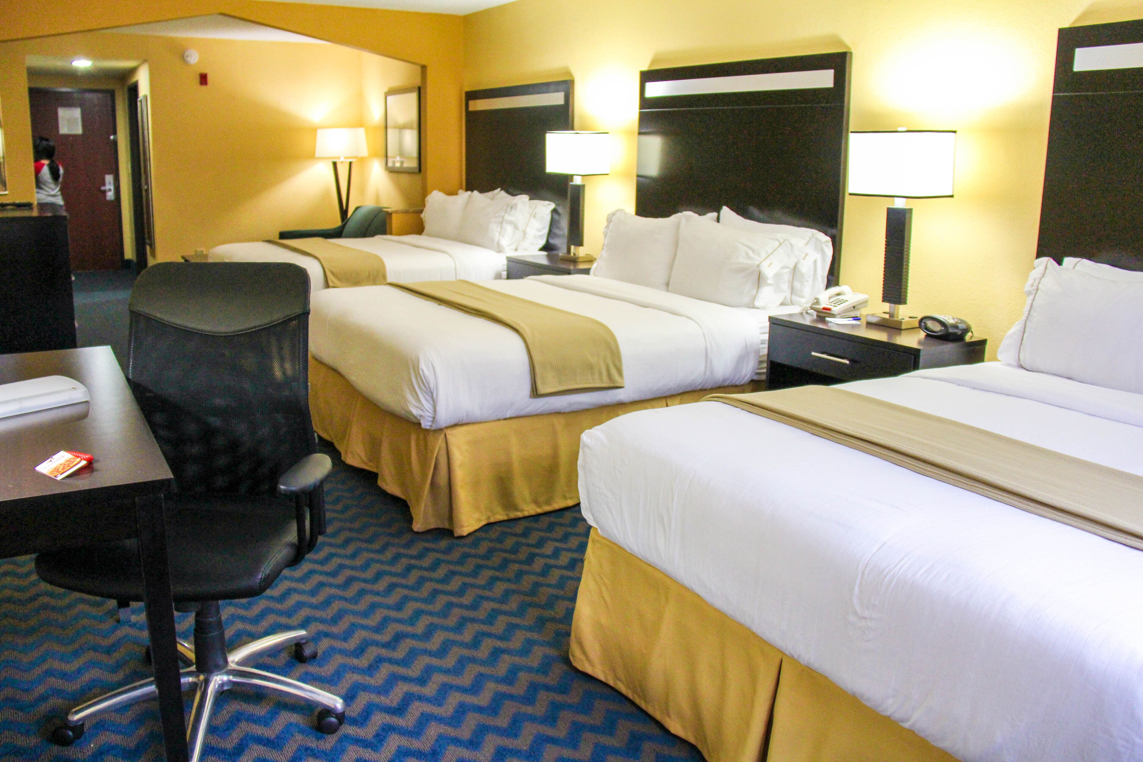 A hotel room with two beds, a desk, a chair, and a telephone.
