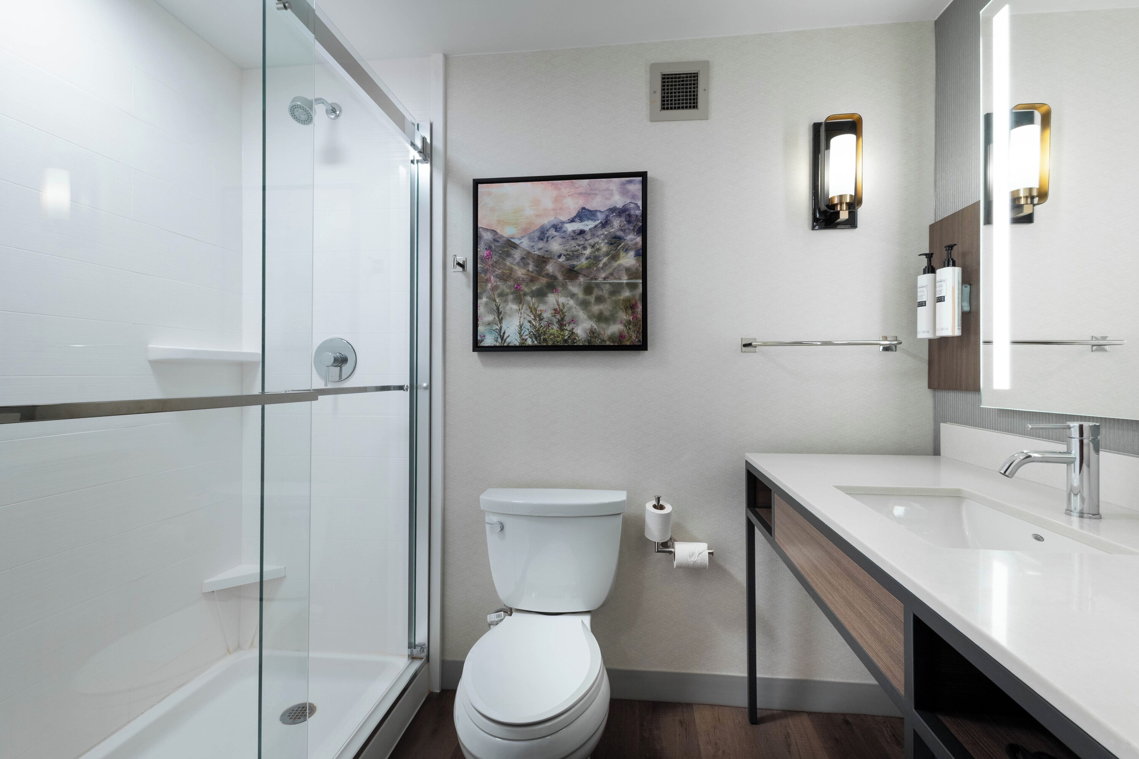 A modern bathroom with a glass shower enclosure, a toilet, a sink with a mirror, and a framed picture on the wall.