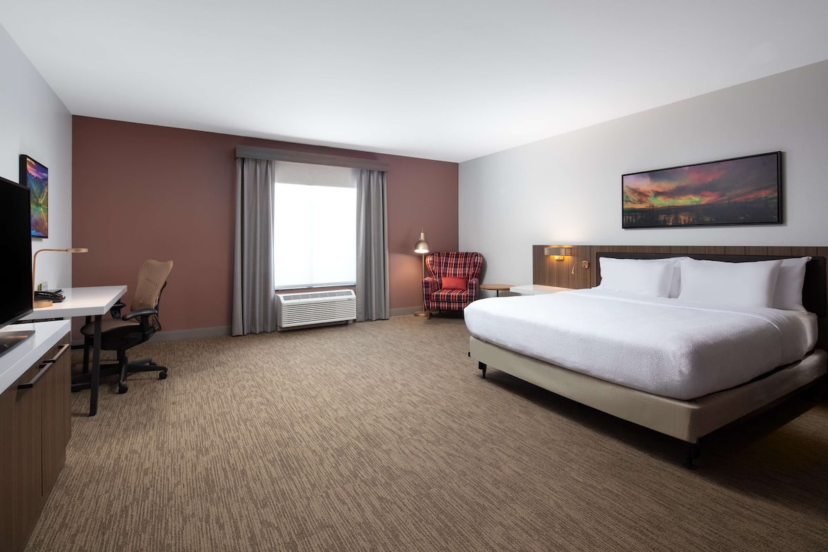 A hotel room with a bed, desk, chair, and a large window with curtains.