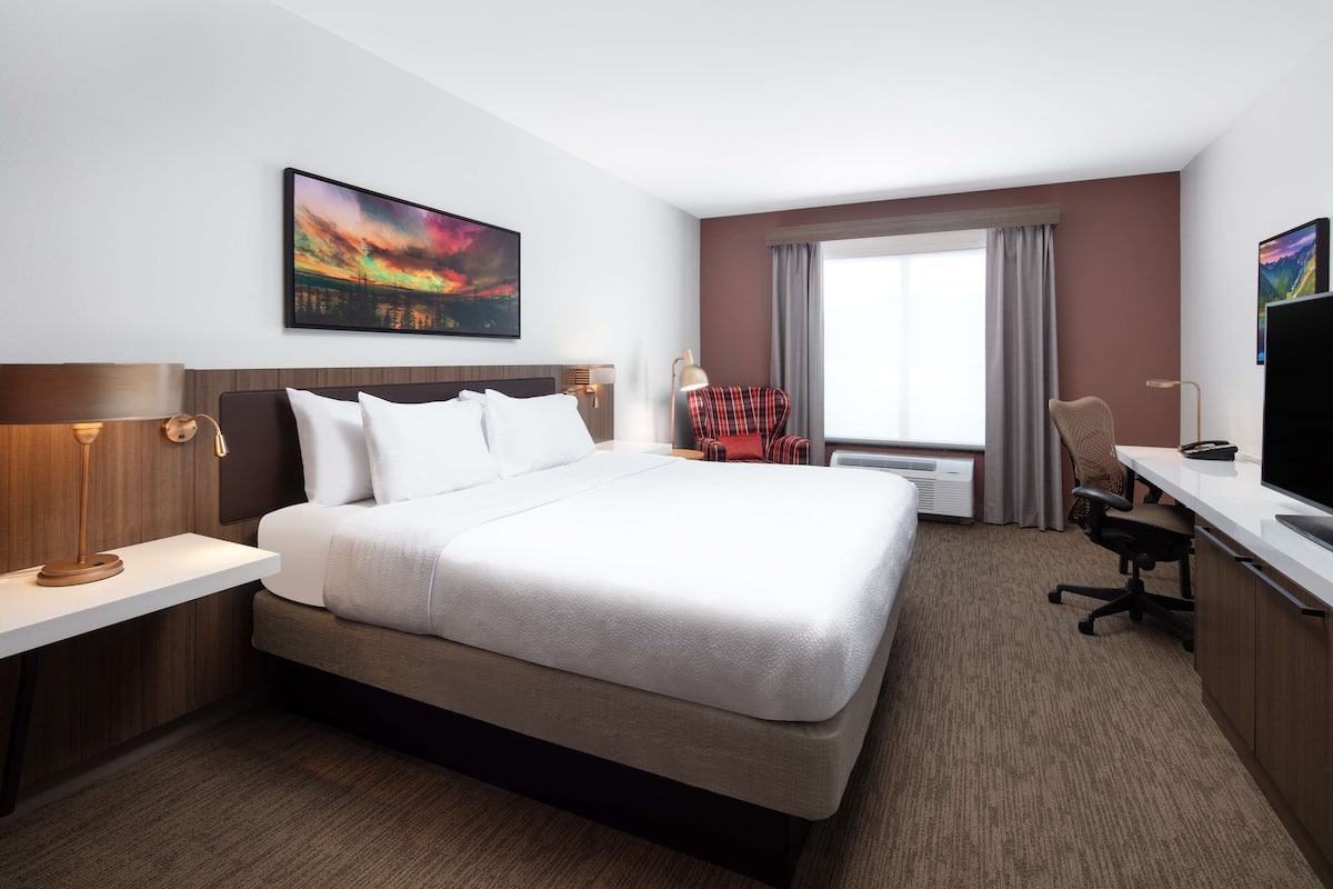 A hotel room with a large bed, a desk with a chair, a TV, and a window with curtains.