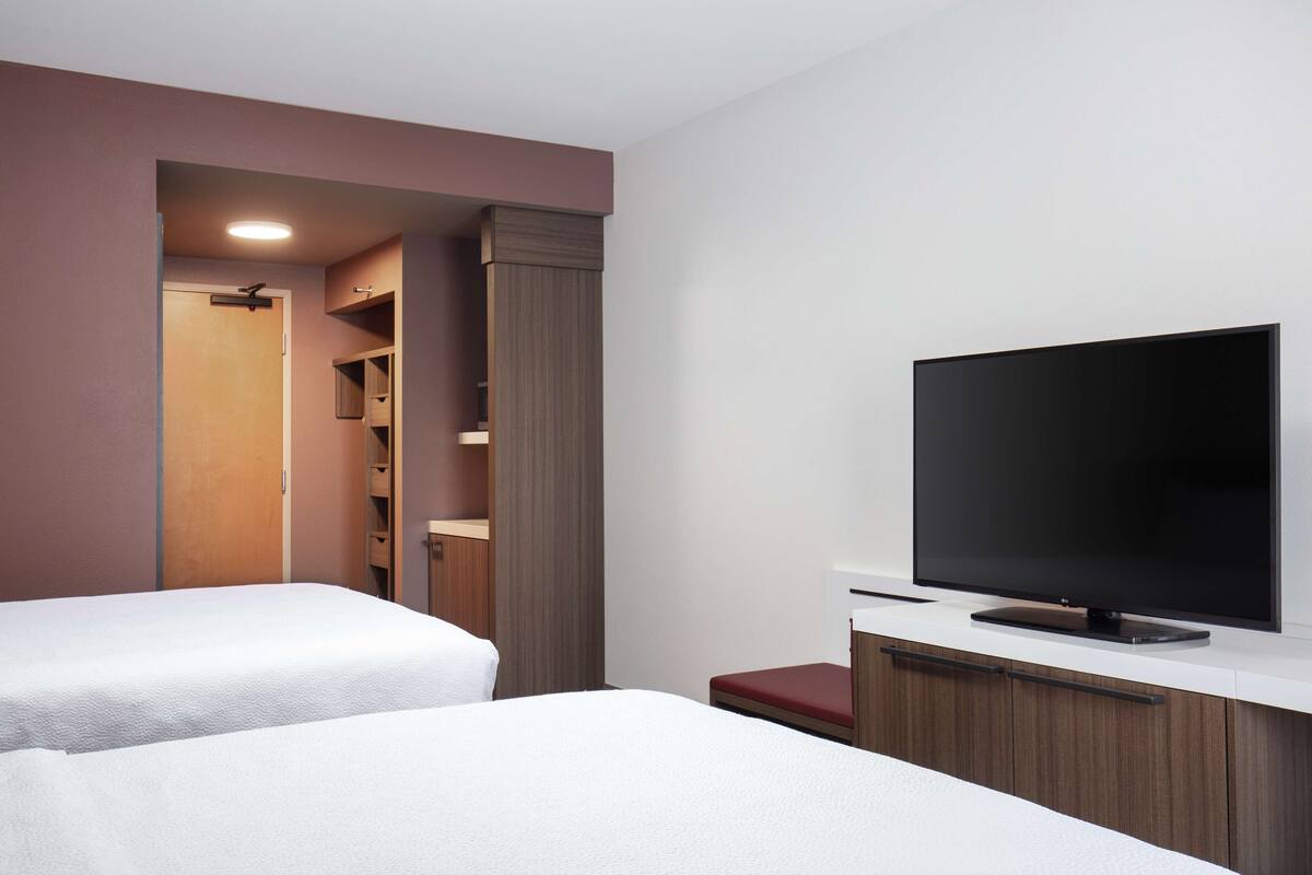 A hotel room with two beds, a TV, a wardrobe, and a closet.