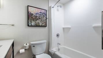 Casa de banho com sanita, chuveiro, banheira e um quadro emoldurado na parede.