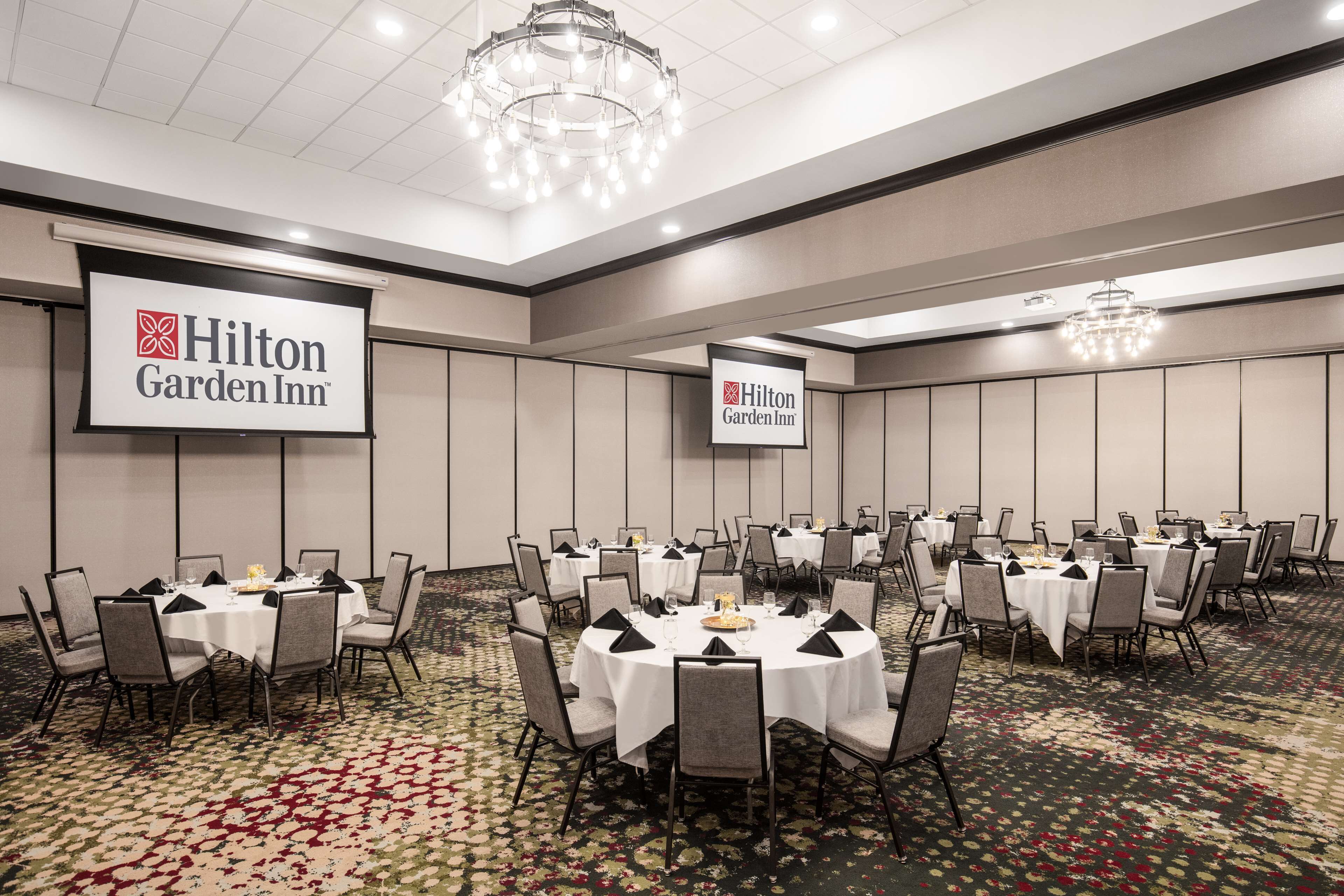 A conference room with multiple round tables, each set with chairs and table settings, at Hilton Garden Inn.