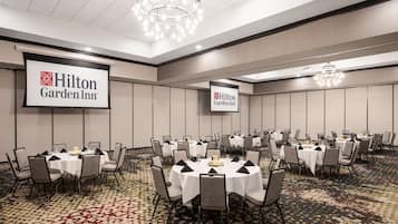 A conference room with multiple round tables, each set with chairs and table settings, at Hilton Garden Inn.