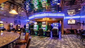 Un casino con numerosas máquinas tragamonedas, una zona de bar y un área de estar con sillas y mesas.