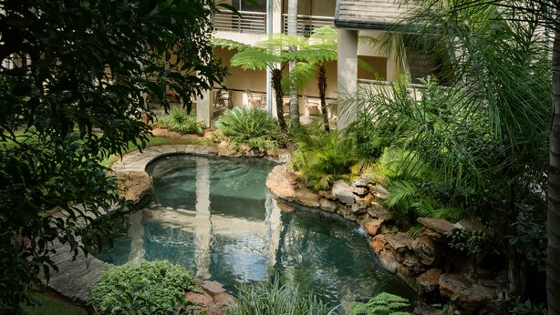 Un jardin intérieur paisible, avec un petit étang, une végétation luxuriante et un sentier en pierre.