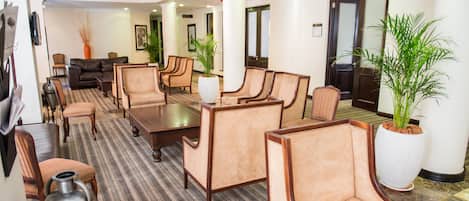A hotel lobby with a seating area, a reception desk, and a large potted plant.