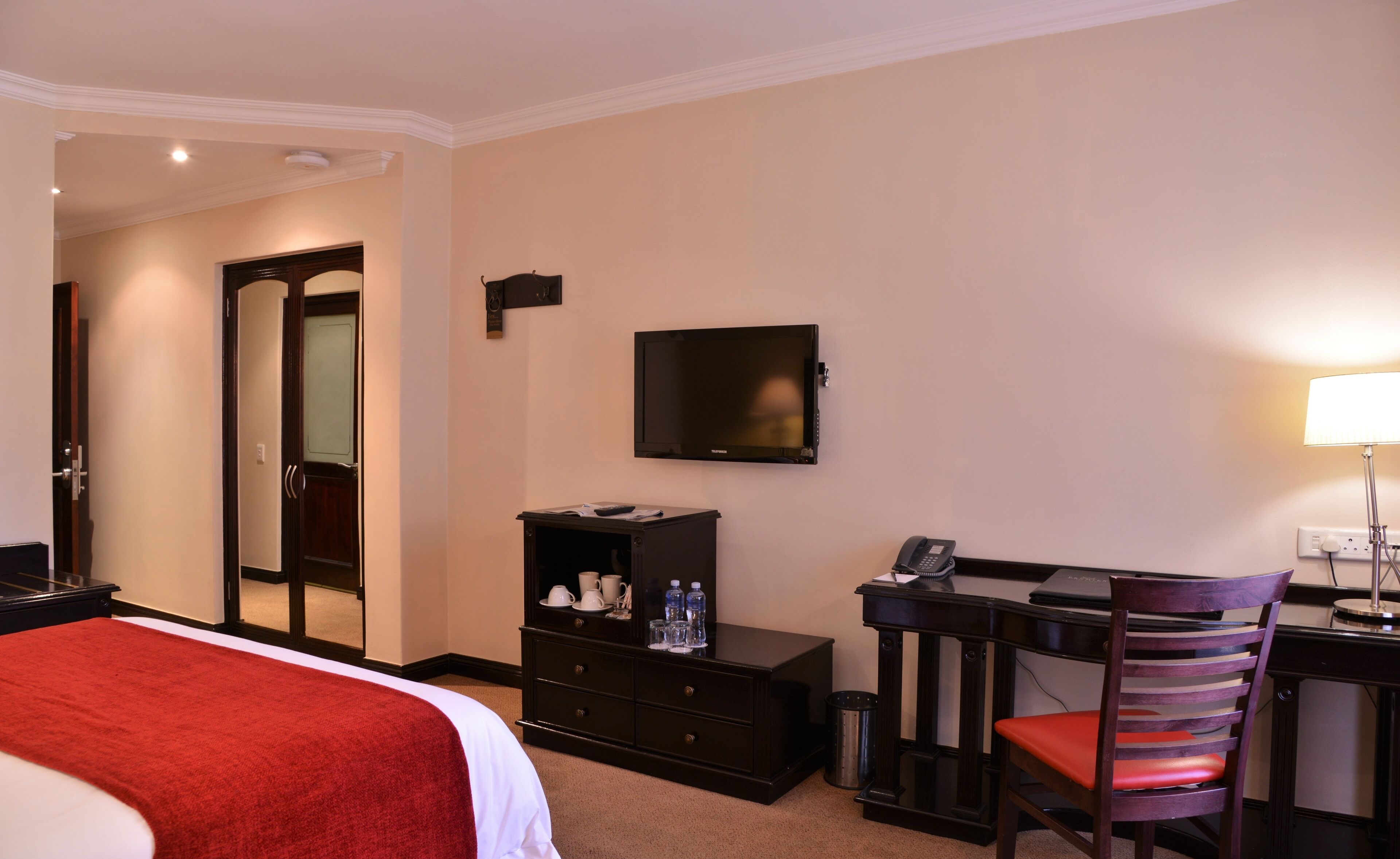 Habitación de hotel con cama, escritorio, silla, televisor, teléfono y espejo.