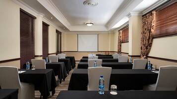 A conference room with multiple tables, chairs, and a projector screen.