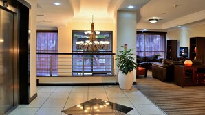 Un hall d’hôtel comprenant une grande plante en pot, un lustre, un téléviseur et un coin salon avec des canapés en cuir.