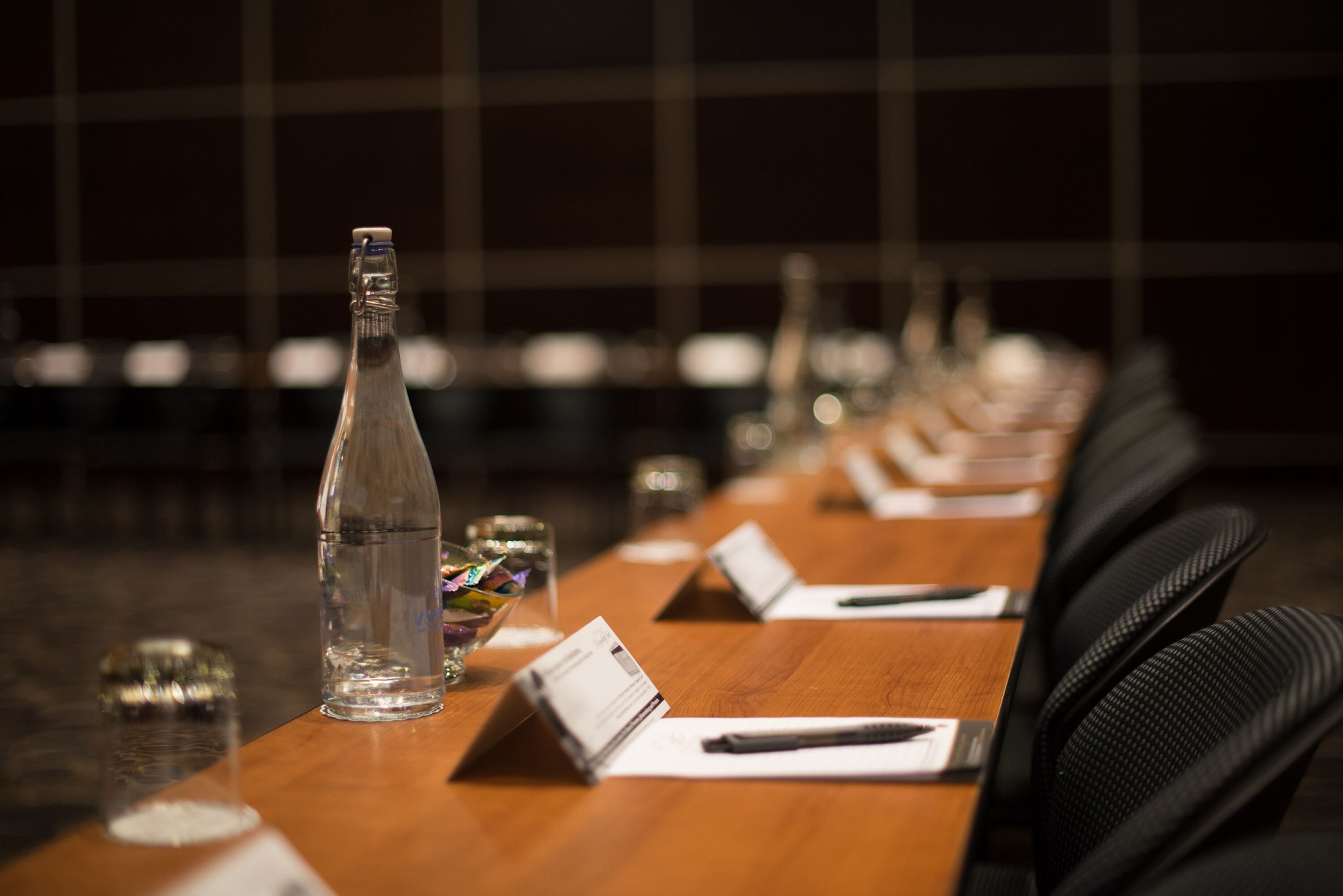 Une table de conférence avec une bouteille d’eau, des porte-noms et des stylos.