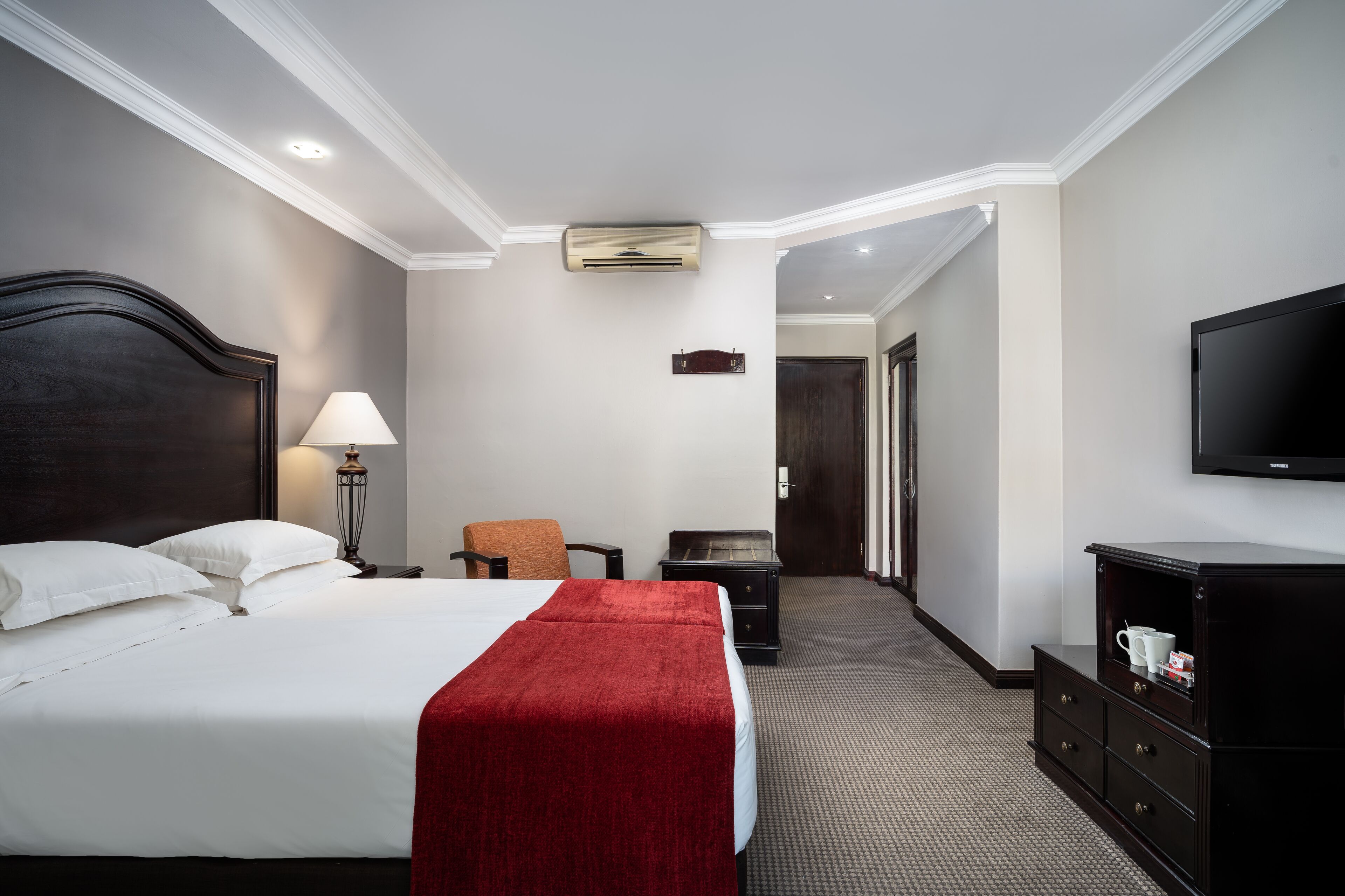 A hotel room with a large bed, a desk, a chair, a TV, and a wardrobe.