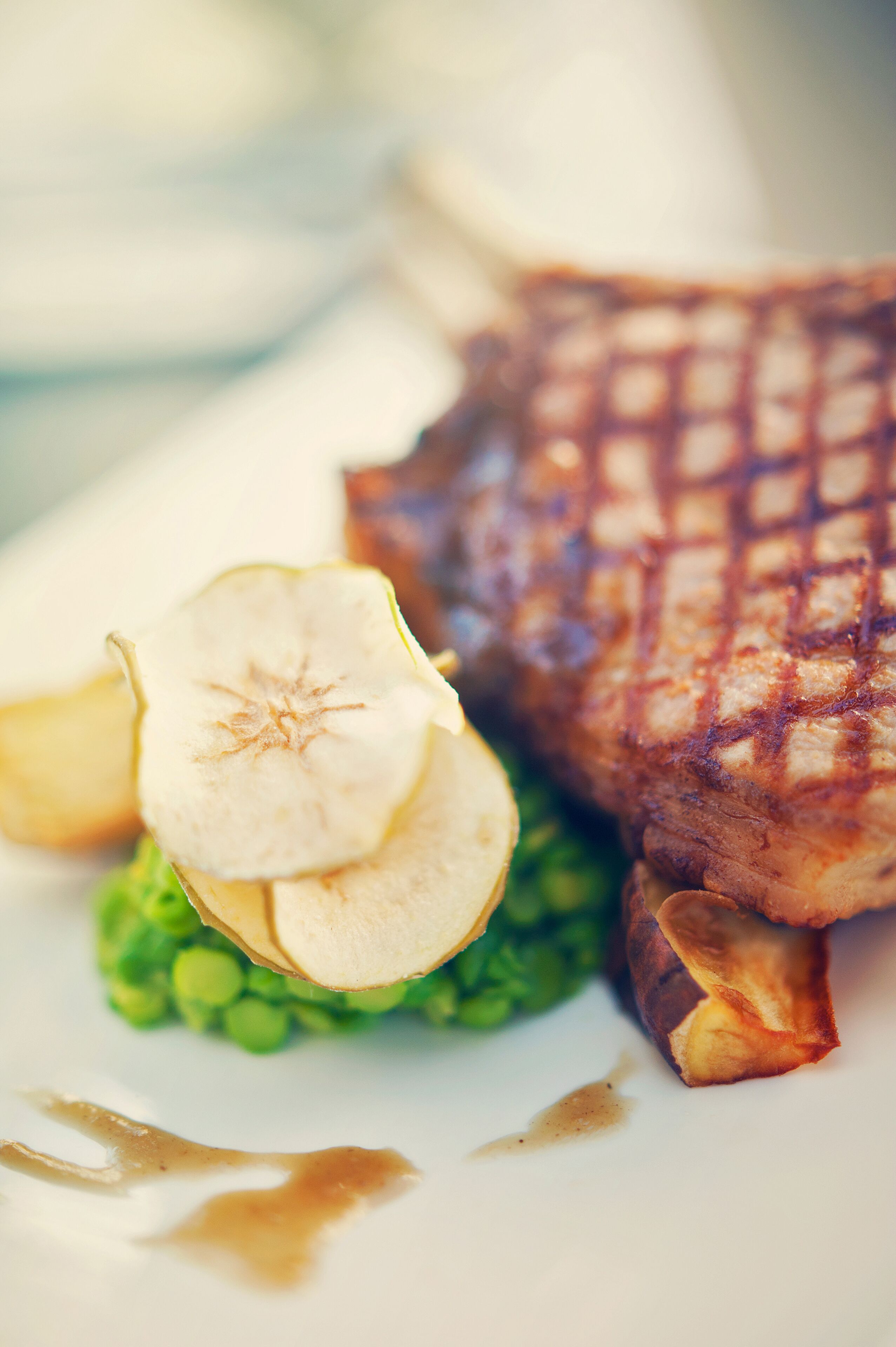 Un plato con un filete a la parrilla, una rodaja de manzana y guisantes verdes.