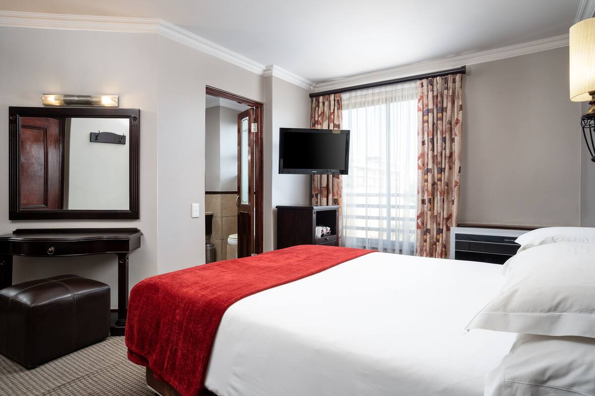 Una camera d'albergo con un letto grande, una scrivania con uno specchio, una TV a schermo piatto e una finestra con tende.