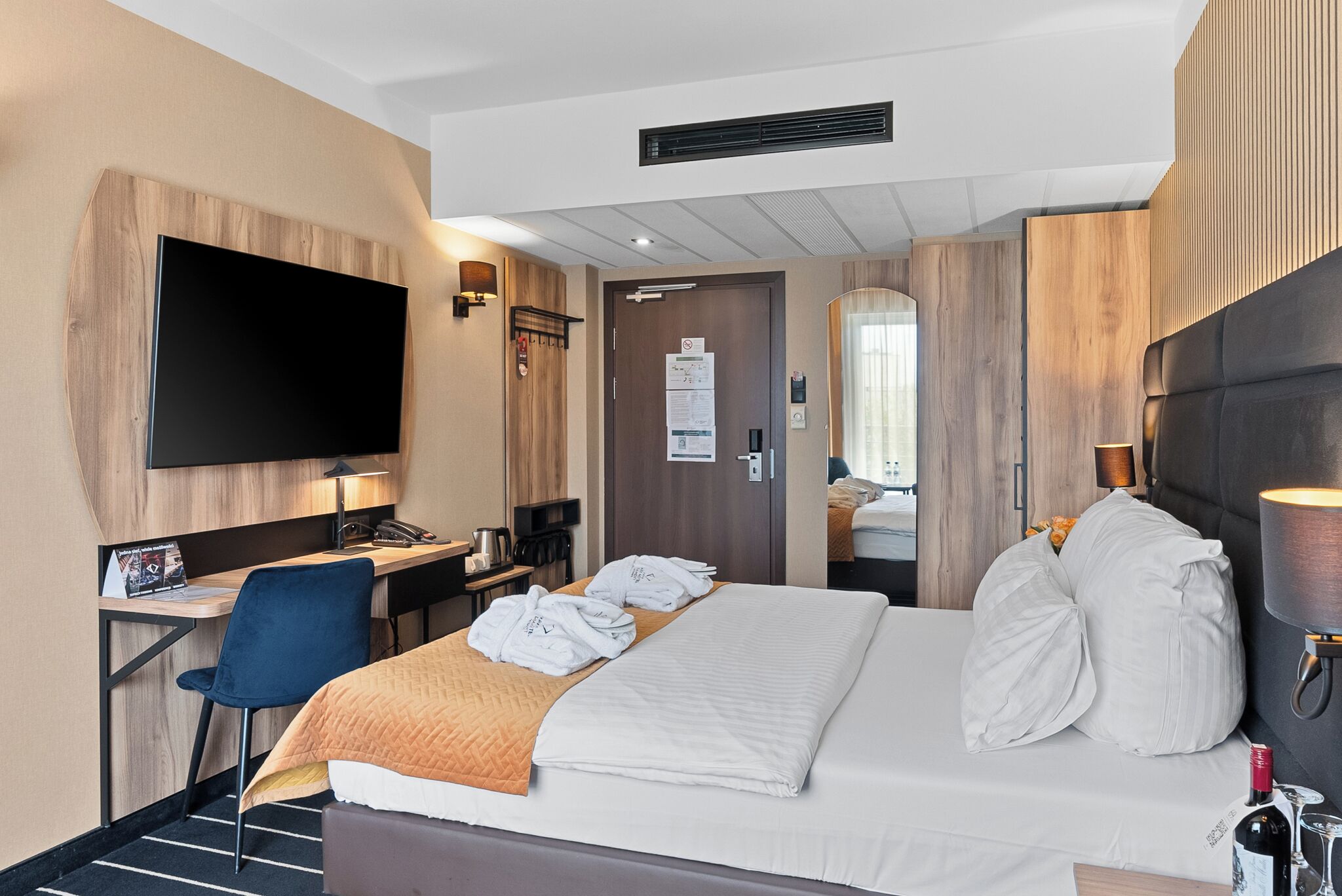 A hotel room with a bed, a desk, a chair, a TV, and a mirror.