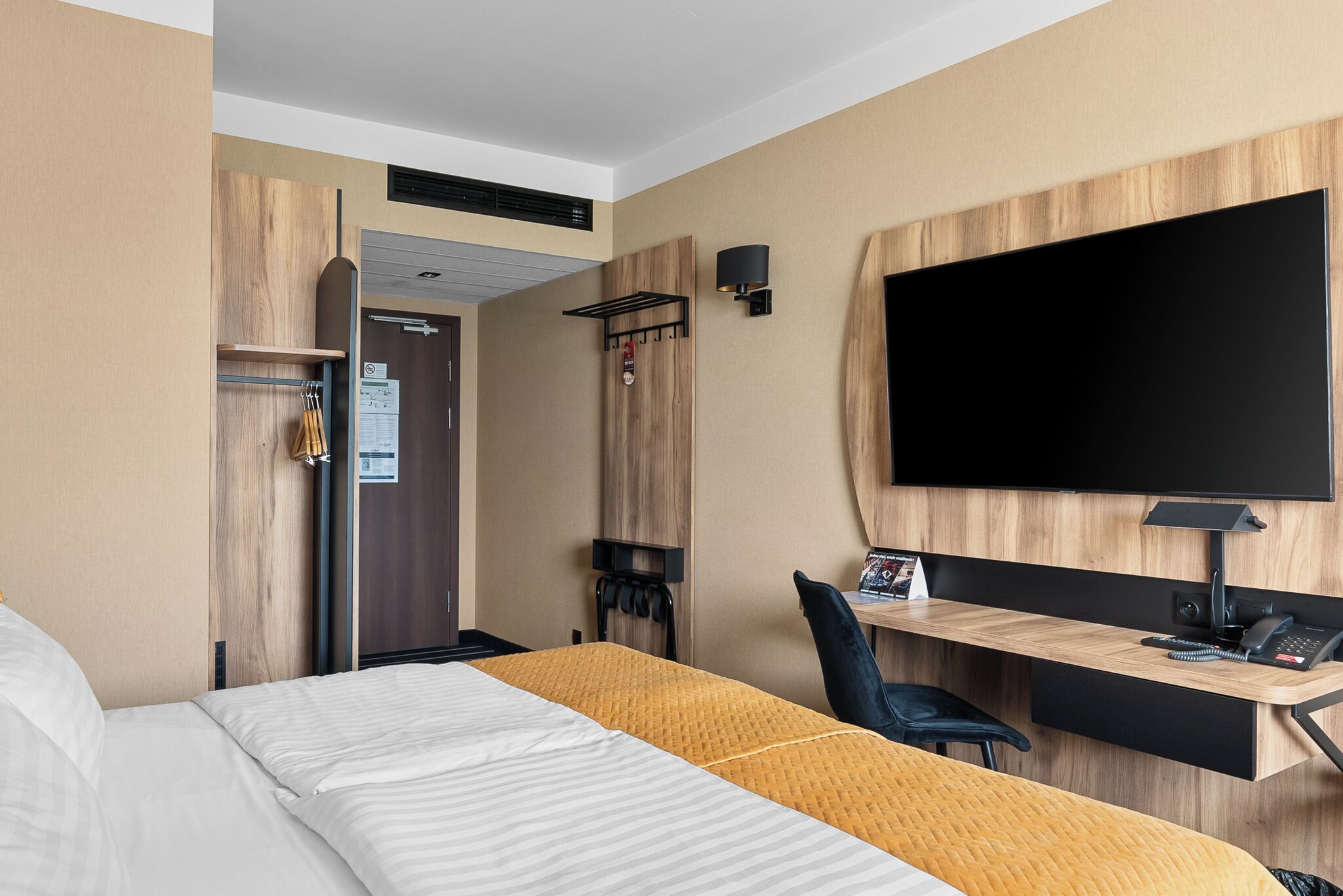 Habitación de hotel con cama, escritorio, televisor y perchero.