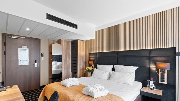 Una habitación de hotel con cama, mesita de noche, lámpara y panel en la pared.