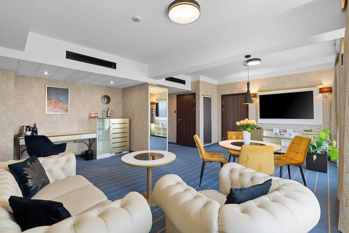 Hotelkamer met een groot bed, een zithoek met een bank en stoelen, een eettafel met stoelen, een televisie en een kleine keukenhoek.