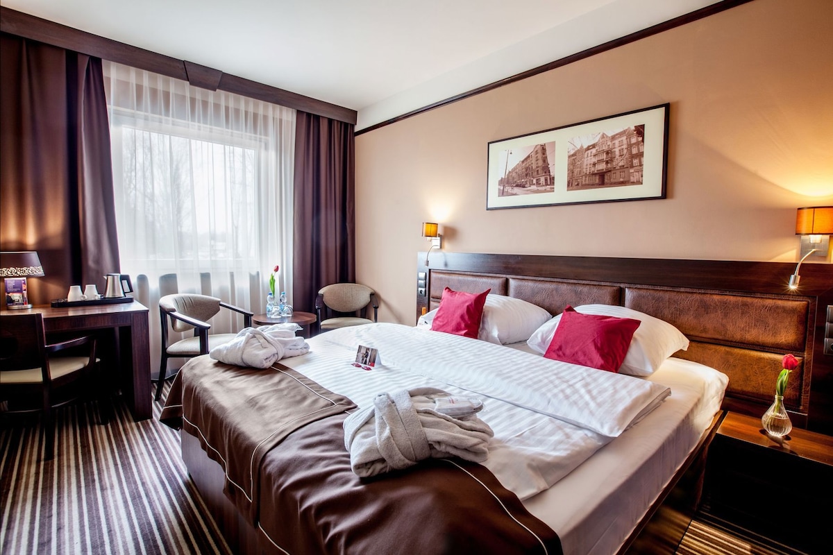 Habitación de hotel con una cama grande, un escritorio, una silla y una mesita de noche.