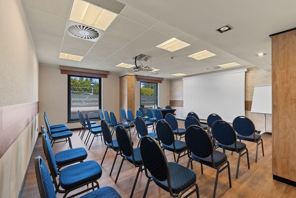 Un salón de conferencias con filas de sillas, una pizarra y un proyector.