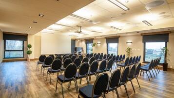A conference room with rows of chairs, large windows, and a wooden floor.
