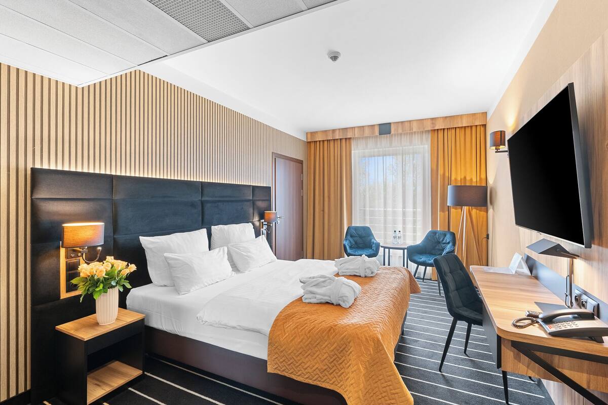 Een hotelkamer met een groot bed, nachtkastjes, een bureau, een stoel, een televisie en een raam met gordijnen.
