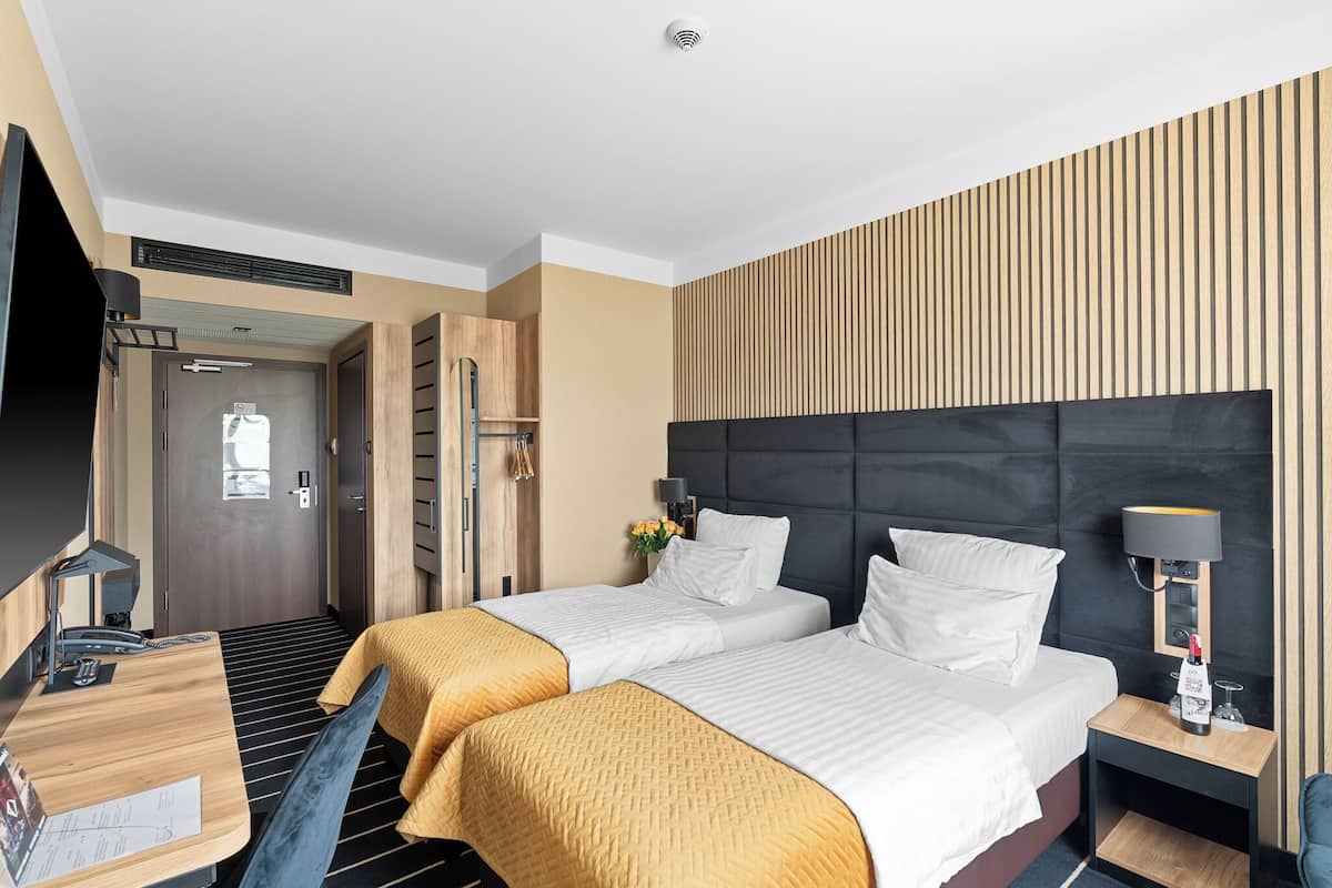 Een hotelkamer met twee bedden, een bureau, een stoel, een nachtkastje en een aan de muur bevestigde televisie.