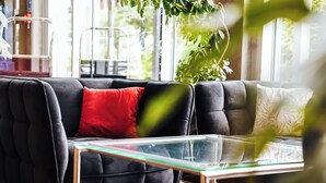 Un salón moderno con un sofá oscuro, una mesa de centro de vidrio y vistas a zonas verdes.