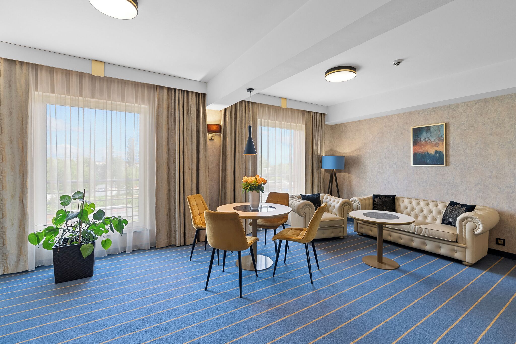 Ett hotellrum med en matplats, en soffa, en krukväxt och en tavla på väggen.