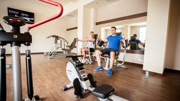 Un gimnasio con máquinas de cardio, espejos y suelo de madera.
