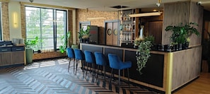 Zona de bar con suelo de espiga, taburetes azules y barra con plantas y botellas.