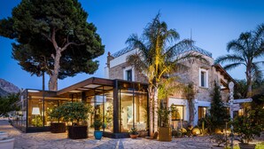A stone building with a glass conservatory, palm trees, and potted plants. - Magaggiari Hotel Resort (Cinisi)