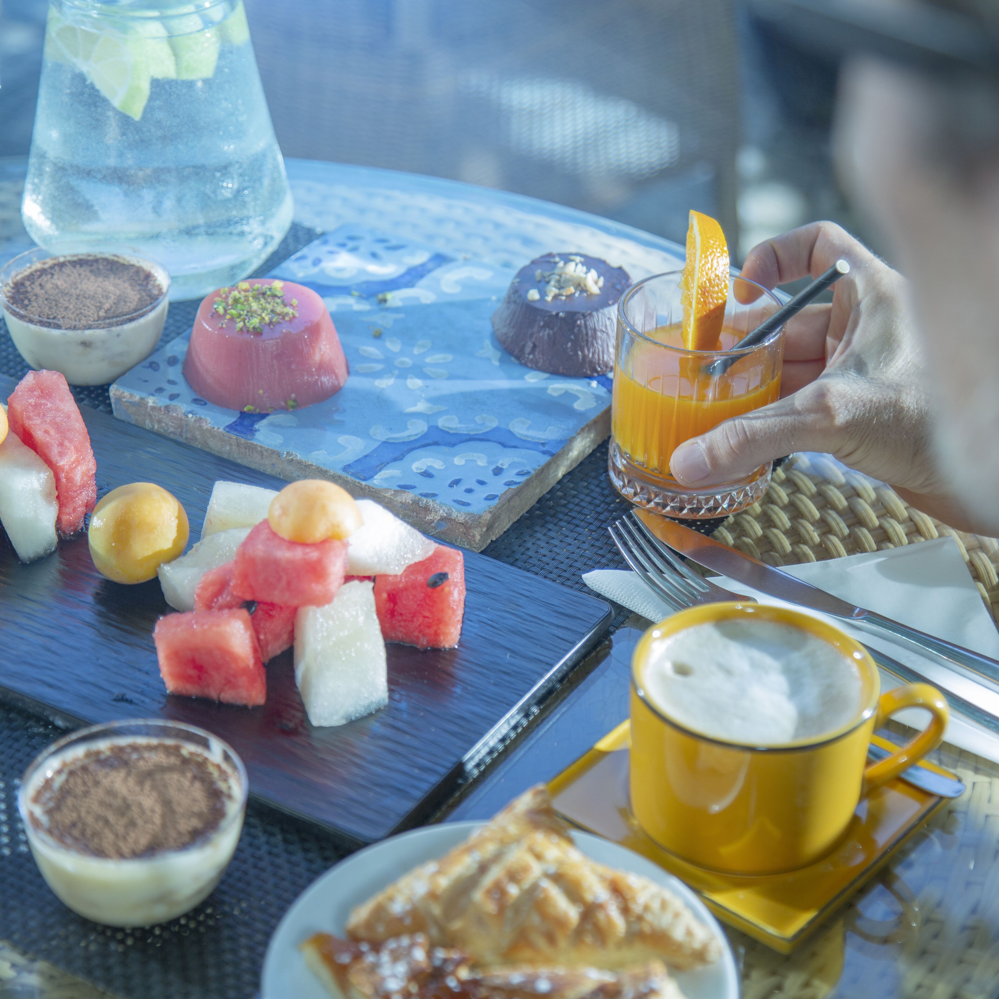 Una mesa con diferentes alimentos, un vaso de zumo de naranja y una taza amarilla, probablemente con café o té.