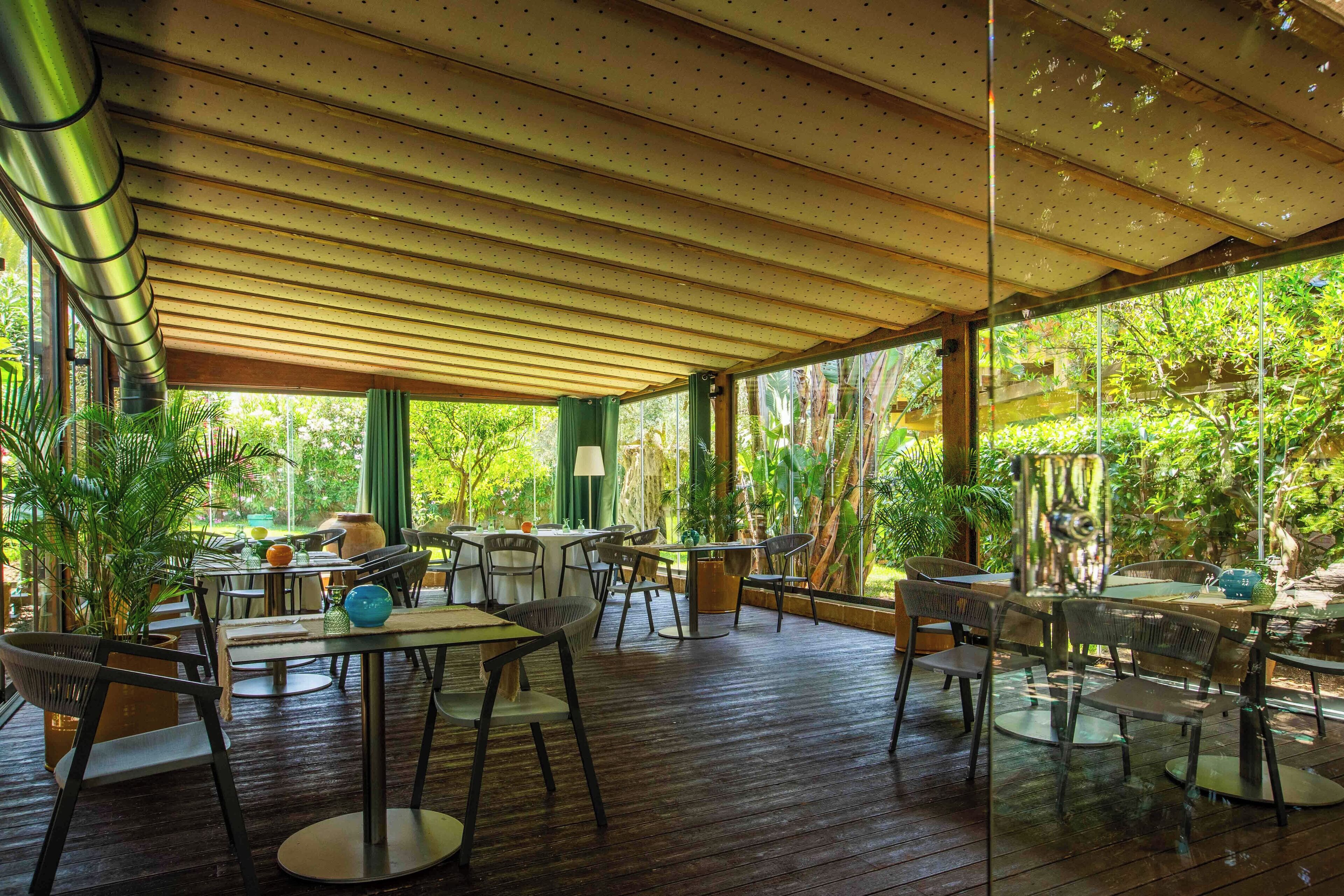 An indoor dining area with wooden flooring, glass partitions, and tables with chairs.